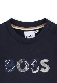 Dark navy t-shirt with ribbed crew neck, featuring "BOSS" logo in embroidered textured patterns and accents of light blue and gold.