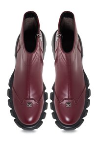 Bottines en cuir bordeaux avec un design épuré, dotées d'une fermeture éclair sur le côté et d'une semelle en caoutchouc noir épaisse avec des rainures texturées.