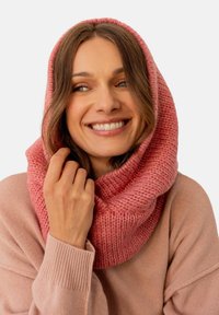 Zdobiony gradientowymi odcieniami różu, dzianinowy szalik w formie infinity o grubej teksturze i szerokim, przytulnym fasonie, noszony na miękkim różowym swetrze.