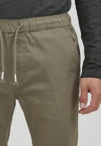 Licht olijfgroene broek met een elastische tailleband, detail met koord en zijzakken. De stof lijkt glad met een licht matte afwerking.