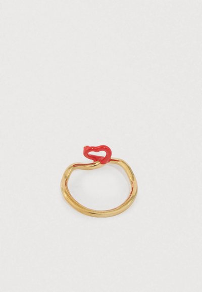 Prsteň v zlatej farbe s hladkým, zakriveným dizajnom; na vrchu je červený akcent v tvare srdca. Kruhový tvar s lesklým povrchom.