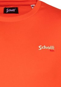 Camiseta de algodón naranja con cuello redondo y mangas cortas, con el logotipo bordado en blanco y rosa "Schott N.Y.C." en el pecho.