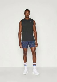 Black sleeveless top, navy shorts with multicolored diagonal stripes, white athletic shoes, and striped white socks. Subtle logo on top.