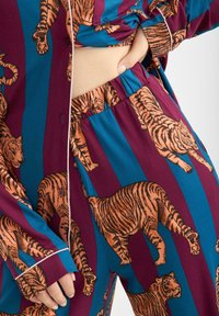 Ensemble de pyjama multicolore avec des motifs de tigres sur un fond bordeaux foncé et bleu. Fabriqué en tissu doux avec un haut boutonné et une taille élastique.