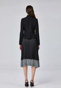 Veste noire ajustée au design structuré. Jupe noire plissée avec un ourlet en dentelle argentée. Sandales noires à talons hauts complètent le look.