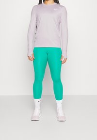 Lilla langærmet træningstrøje, teal leggings, hvide sokker og lyserøde sneakers. Har logo på trøjen og tætsiddende leggings.