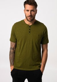 Camisa henley de manga corta en verde olivo con cuello redondo, tapeta de tres botones y un bolsillo en el pecho, hecha de una suave tela texturizada.