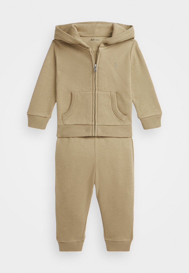 Bezsarkanu kokvilnas sporta jaku ar rāvējloku un priekšējiem kabatām, apvienota ar atbilstošiem sporta biksēm ar ribotām siksnām. Vienkāršs dizains bez rakstiem.