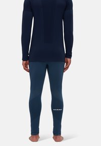 Person steht barfuß, trägt ein marineblaues Langarmoberteil und dunkelblaue, enge Leggings mit dem "MAMMUT"-Logo an der unteren Wade.