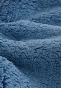 Soft, textured fabric with a plush, curly surface in a muted blue color, shown in close-up with light and shadow details.
