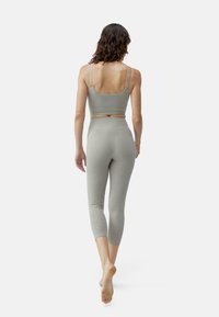 Lichtgrijze actieve kleding set met een sportieve bralette met dunne bandjes en hoge, cropped legging, gemaakt van een gladde, gestructureerde stof.
