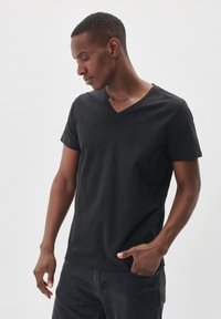 T-shirt nera con scollo a V in morbido cotone, design aderente, maniche corte e texture liscia. Abbinata a jeans scuri.