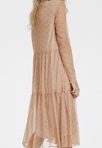 Lång, lager-på-lager klänning i genomskinlig, lätt tyg med ett pastellblommönster. Har långa ärmar och en avslappnad passform, som flödar ner till mitten av vadbenet.