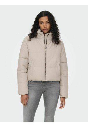 Giacca a vento in beige chiaro con colletto alto, zip frontale e design trapuntato. Abbinata a jeans grigi, mostra un look casual.