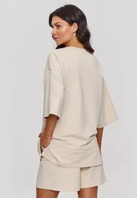 Beżowy, oversize T-shirt z szerokimi rękawami, wykonany z miękkiego bawełnianego materiału, z bocznymi rozcięciami, w połączeniu z pasującymi szortami dla uzyskania swobodnego wyglądu.