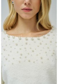 Maglione bianco lavorato a maglia con scollatura arrotondata, decorato con perle grandi e piccole sparse. Texture morbida con un aspetto accogliente.