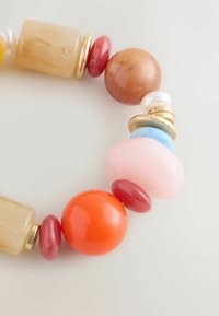 Krāsains pērlīšu rokassprādze, kas satur apaļas, ovālas un taisnstūra formas pērlītes no sveķiem un stikla, ar zelta akcentiem un dažādām tekstūrām.