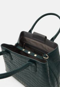 Zelená kabelka typu tote s texturou a krokodýlím raženým vzorem, zlatým kováním a dvěma horními uchy. Vnitřek obsahuje kapsu na zip a zapínání na knoflík.