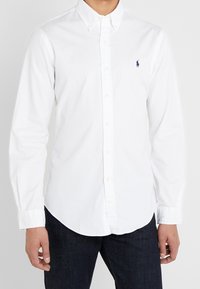 Biała bawełniana koszula zapinana na guziki, z długimi rękawami, klasycznym kołnierzykiem i małym haftowanym logo na lewej piersi.