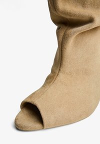Beige velúr, nyitott orrú csizma laza dizájnnal, sima textúrával és ívelt sziluettel. Puha felület kiemeli az anyagot.