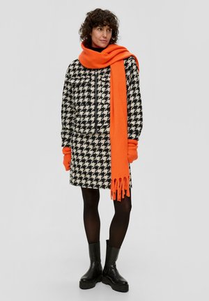 Zwart-wit houndstooth jasje en rok, gecombineerd met een oranje sjaal. Model draagt zwarte panty’s en chunky zwarte enkellaarsjes.