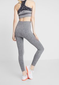 Szare, elastyczne legginsy w połączeniu ze sportowym stanikiem w wzory i białymi sneakersami z pomarańczowymi akcentami, ukazującymi dopasowany krój i gładką teksturę.