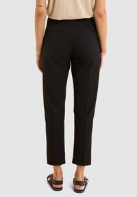 Pantalons noirs ajustés avec une coupe slim, devant plat et jambes droites. Portés avec un haut beige texturé et des sandales noires. Vue arrière.