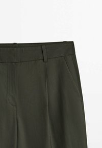 Pantalon vert foncé à texture lisse, doté d'une ceinture plate, de poches latérales et d'une coupe ajustée. Le tissu est léger et légèrement brillant.