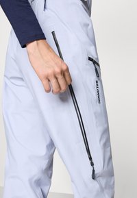 Vodoodporne bele smučarske hlače z črnimi žepi na zadrgo, ki se ponašajo s sleek dizajnom in dihanjem prijaznim materialom za udobje in gibljivost.