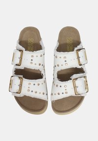Sandalias blancas con dos hebillas ajustables, acentos de tachuelas, bordes de tela deshilachados y una plantilla acolchada color marrón.