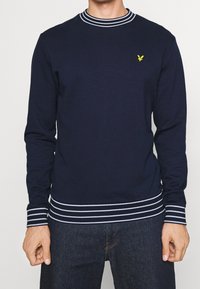 Felpa blu navy con maniche lunghe, colletto e polsini a righe bianche, con un piccolo logo giallo sul petto. Materiale misto cotone.