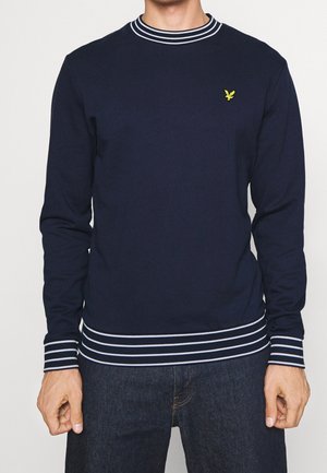 Sweatshirt bleu marine à manches longues, col et poignets rayés blancs, avec un petit logo jaune sur la poitrine. Matière en mélange de coton.