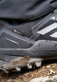Czarne buty trekkingowe z teksturowaną powierzchnią, wodoodpornym materiałem GORE-TEX, wytrzymałą podeszwą oraz nagromadzeniem brudu na zewnętrznej podeszwie.