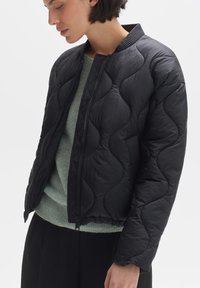 Zwarte gewatteerde pufferjack met een geribde kraag en ritssluiting. Heeft een textuurpatroon met gebogen naden en is gemaakt van lichtgewicht materiaal.