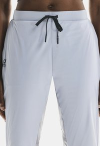 Pantalones deportivos de color gris claro con cierre de cordón y acentos negros, con una tela suave y liviana y un diseño ajustado.