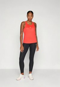 Rød atletisk tanktopp med racerback-design, kombinert med svarte leggings. Hvite joggesko med lilla og rosa detaljer. Jevn tekstur overalt.