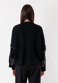 Maglione nero lavorato a maglia con texture a coste e dettagli di paillettes sulle maniche. Vestibilità ampia con scollo rotondo e spalle scese.