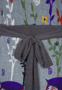 Ceinture en tissu gris nouée en un nœud autour d'une robe gris clair avec des motifs floraux multicolores et des hiboux.