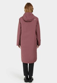 Long, mauve waterproof coat with a hood, relaxed fit, and vented sleeves, paired with black pants and ankle boots, minimalistic design.