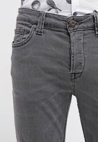 Jeans de denim gris con un corte ajustado, que cuentan con un cierre de botón, bolsillos frontales y patrones de desgaste sutiles. Tejido ligero y texturizado.