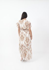 Maxikjole i hvid med brune blomster mønstre, korte puffede ærmer og en indsnævret talje. Stoffet fremstår blødt og let.