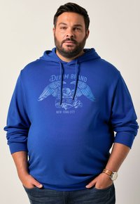 Sudadera con capucha azul con un estampado gráfico que presenta un diseño de águila y texto. Tejido de mezcla de algodón, mangas largas, corte relajado.