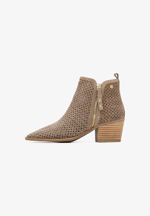 Bota de ante marrón perforada hasta el tobillo con puntera puntiaguda, cremallera lateral y tacón de madera apilado. Presenta recortes geométricos para ventilación.