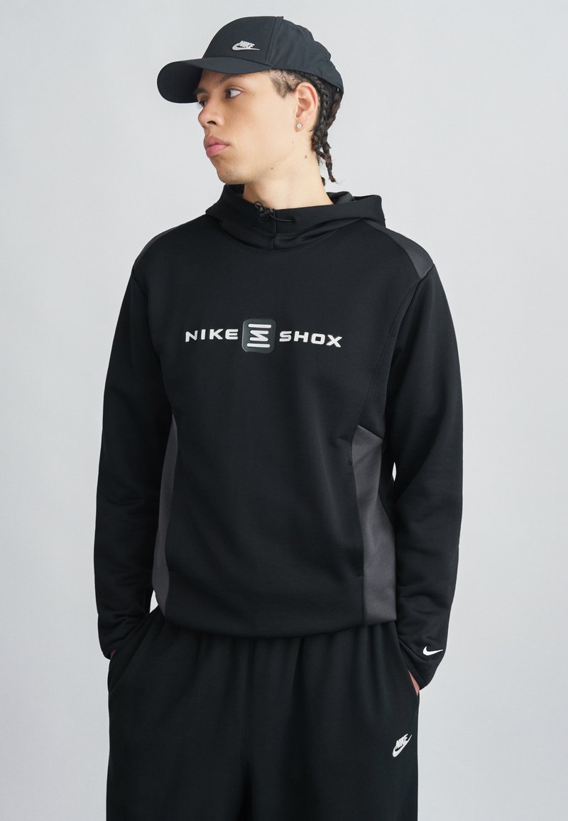 Μαύρο φούτερ Nike με το λογότυπο "NIKE SHOX" σε λευκό, με φερμουάρ στο γιακά, πλαϊνές επενδύσεις και μαύρο παντελόνι φόρμας που ταιριάζει.