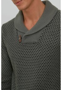 Suéter gris de punto con un patrón texturizado, que presenta un amplio cuello de chal y un acento de botón de madera.