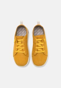 Żółte zamszowe sneakersy z okrągłym noskiem, wiązanym projektem, białą gumową podeszwą i wyściełanym szarym wnętrzem. Pętle z tyłu ułatwiają zakładanie.