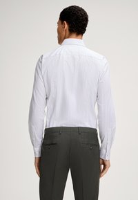 Camicia a maniche lunghe a righe bianche con colletto aperto, abbinata a pantaloni grigi scuri con una texture liscia e tasche posteriori con bottone.
