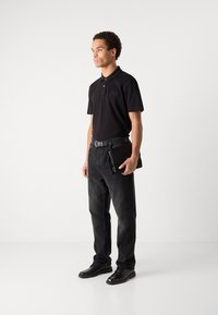 Črna polo majica s kratkimi rokavi, v kombinaciji z temno modrimi jeans hlačami in črnimi čevlji. Pas ima srebrno zaponko. Preprost, sodoben dizajn.