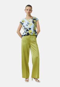 Floral short-sleeve blouse in blue, yellow, and black paired with green satin wide-leg pants and white strappy heels. Elegant design and fit.