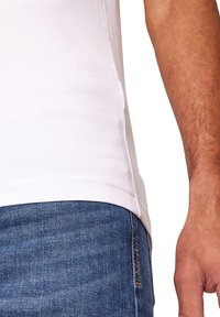 Weißes Baumwoll-T-Shirt mit geradem Schnitt, seitlichen Nähten und glatter Textur, kombiniert mit blauen Jeans und detaillierter Naht.